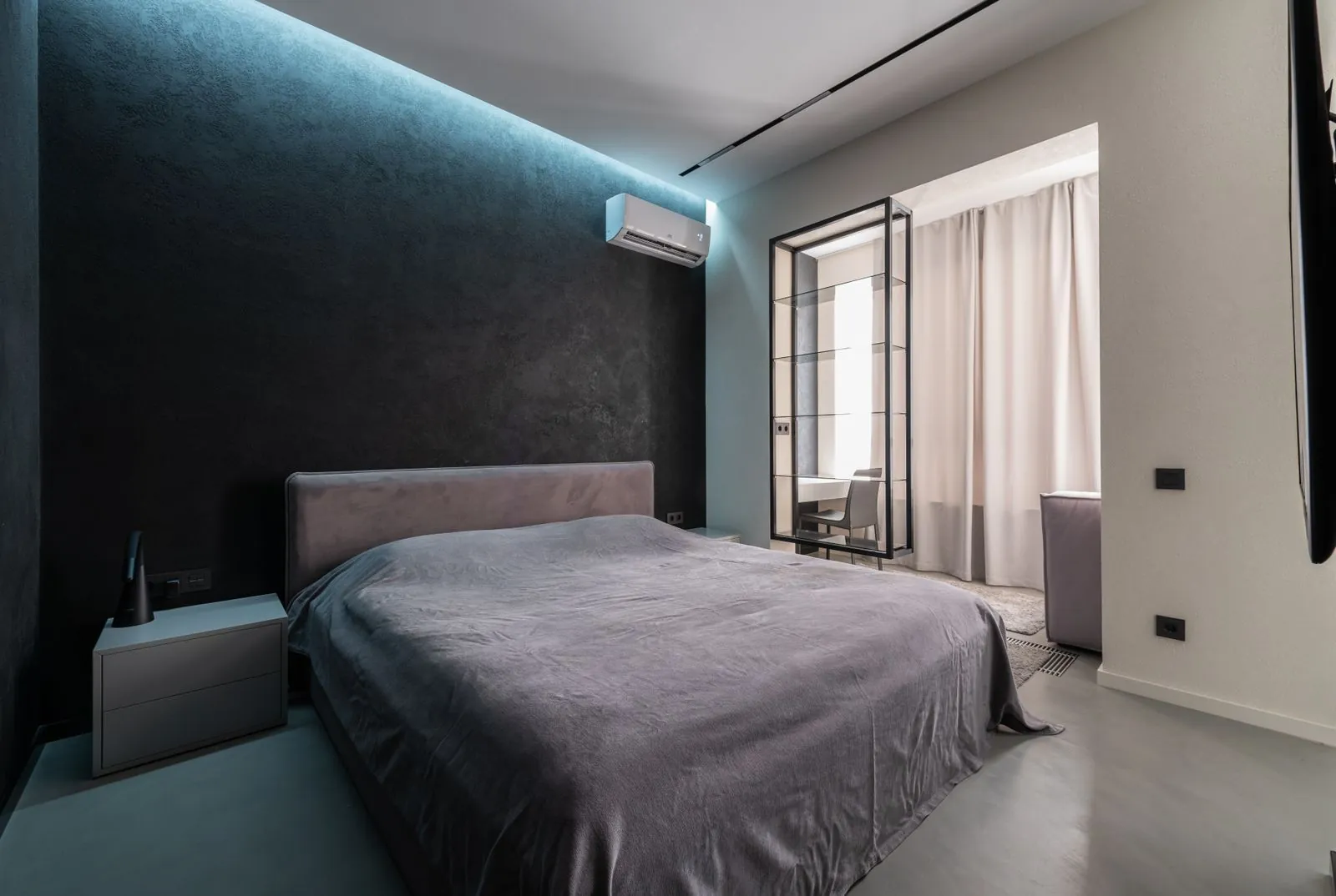 Quarto com unidade de ar condicionado mural instalada por cima da cama, com luz indireta na parede escura